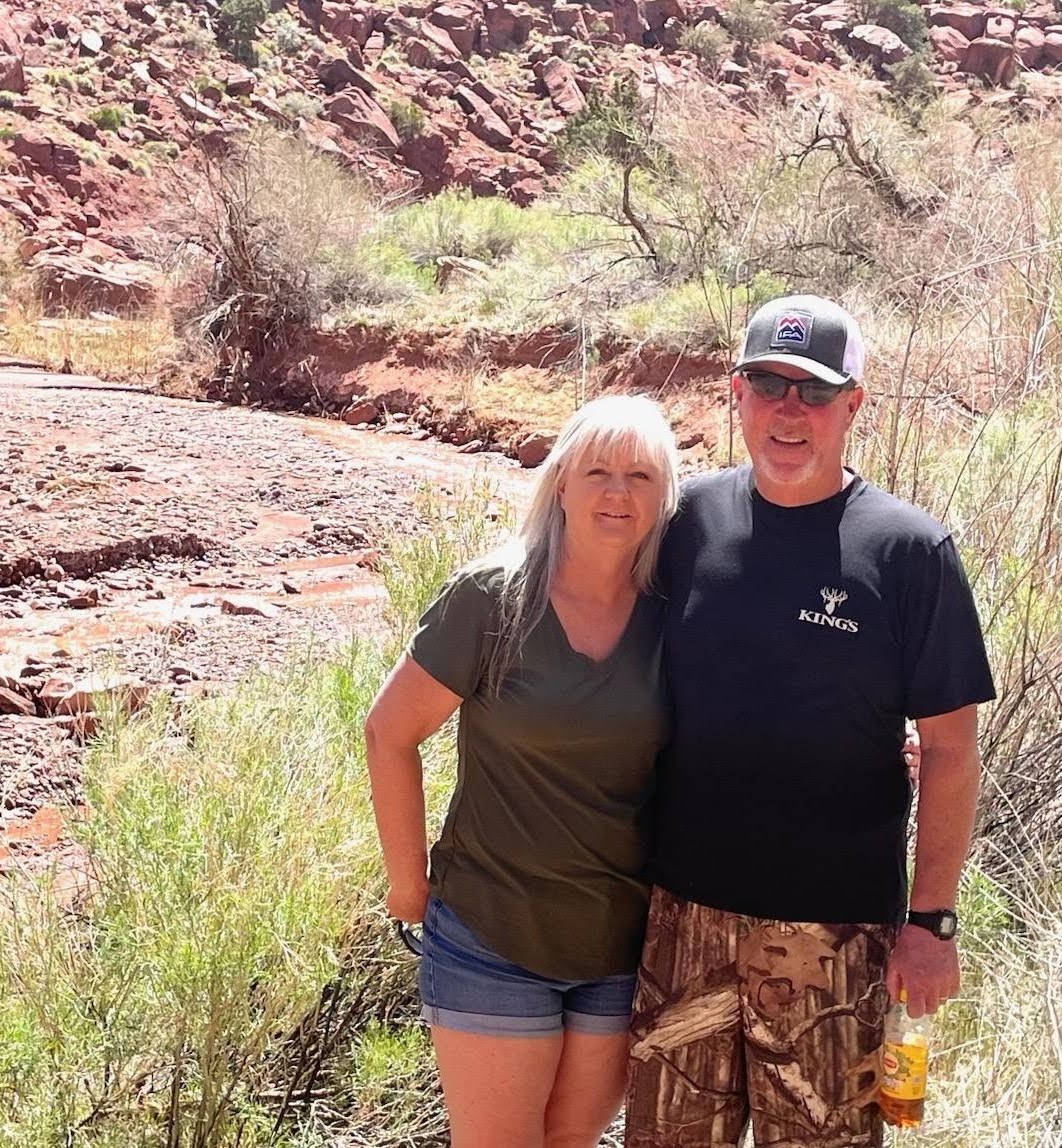 Debbie smiling together with a man in front of of a desert canyon landscape.