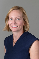 Emily, who has short blonde hair, smiles for a professional headshot.