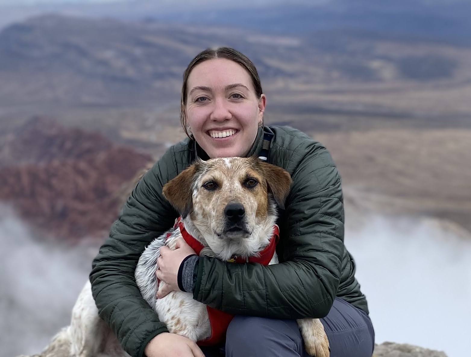 Karen smiles and hugs her dog in front of a blurred mountain background.