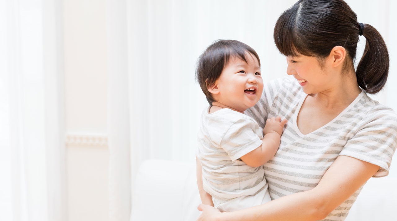Smiling woman holding a laughing baby, both wearing striped shirts in a bright room.